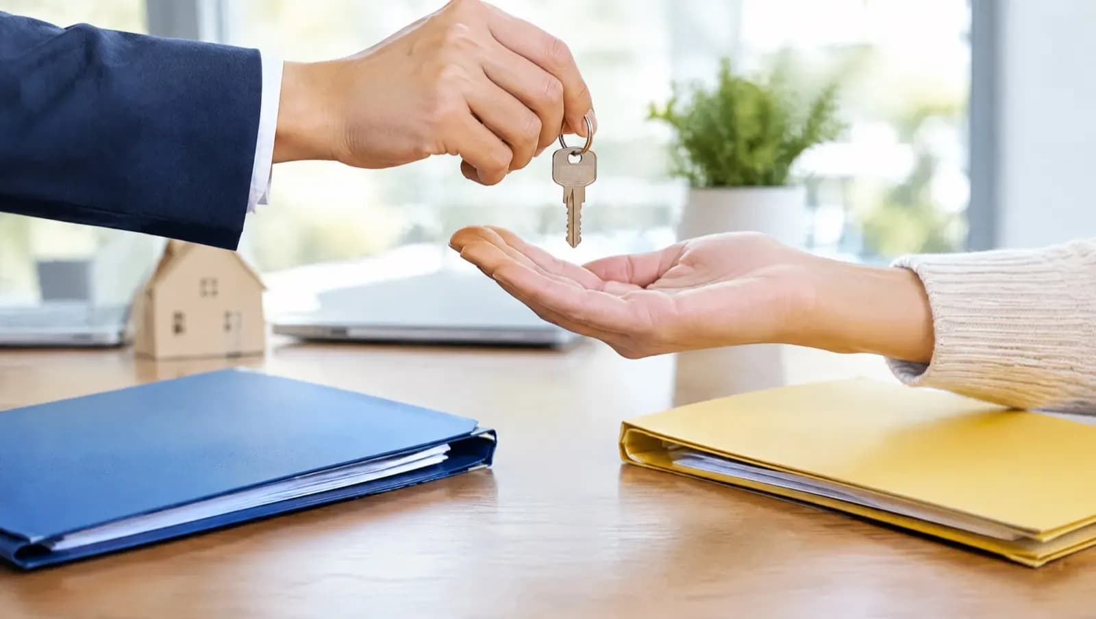 Przekazanie klucza nad biurkiem między dwiema teczkami z ofertami